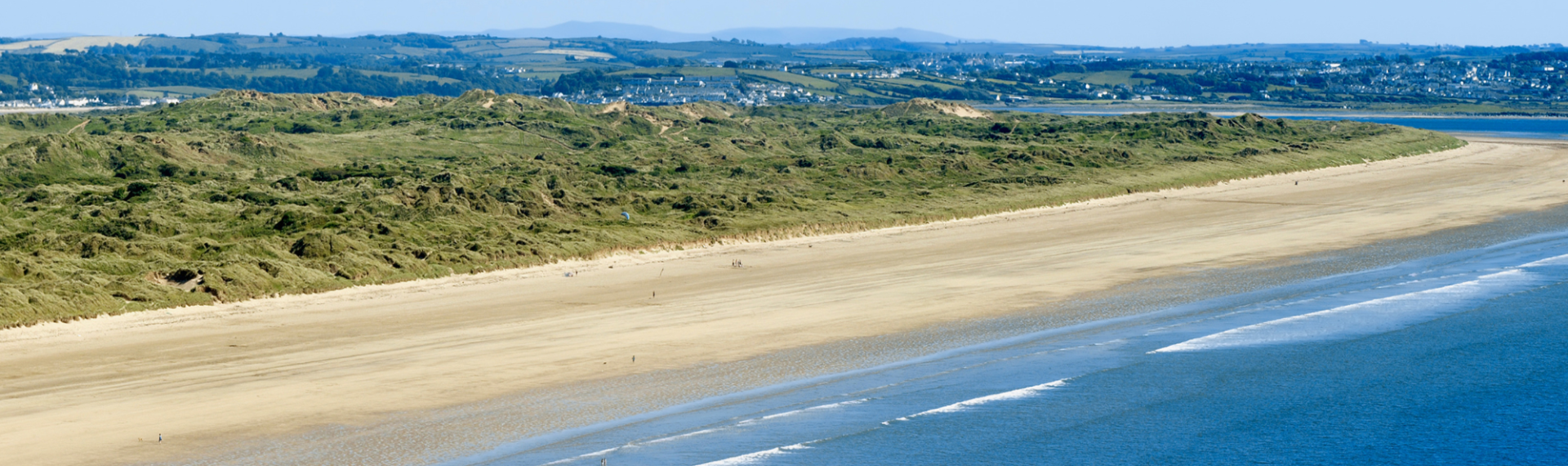 Saunton Sands beach with the sea, sand and green bank behind it in the distance
