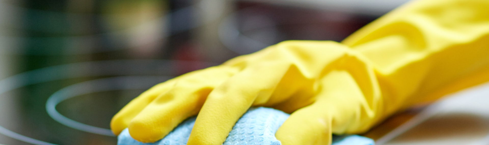 A hand wearing a rubber glove holding a blue cloth on a ceramic hob