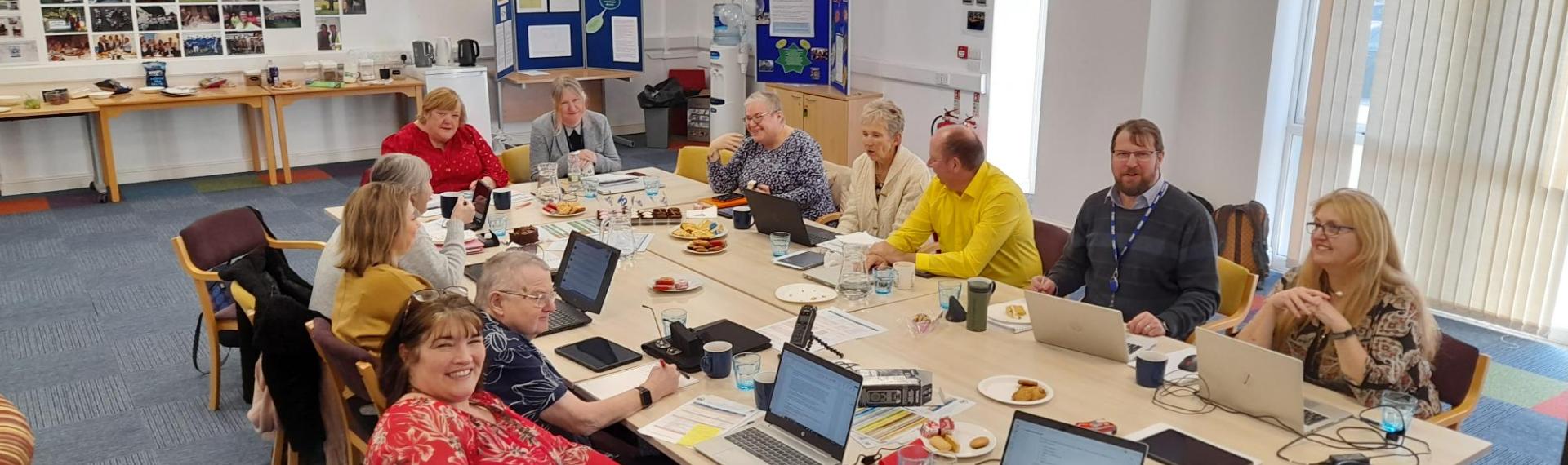 A group of people sat around a meeting table with laptops and snacks