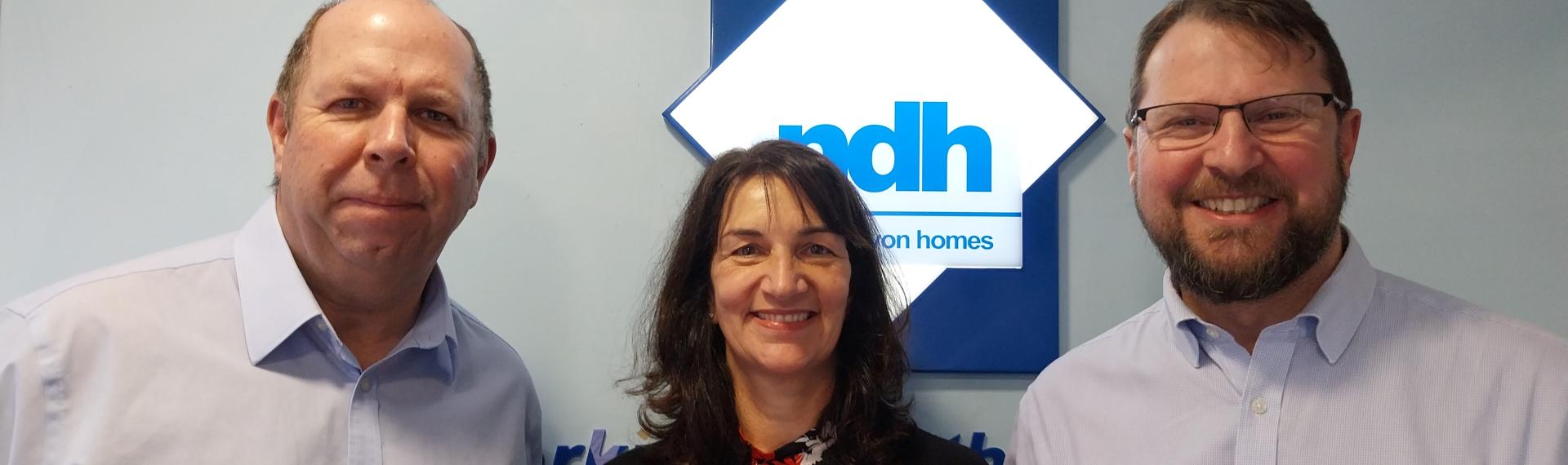 A woman standing between two men in front of an NDH sign