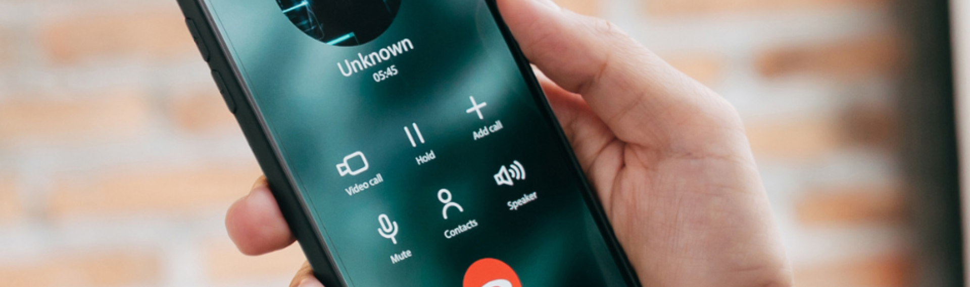 A hand holding a mobile phone showing a call from an unknown caller