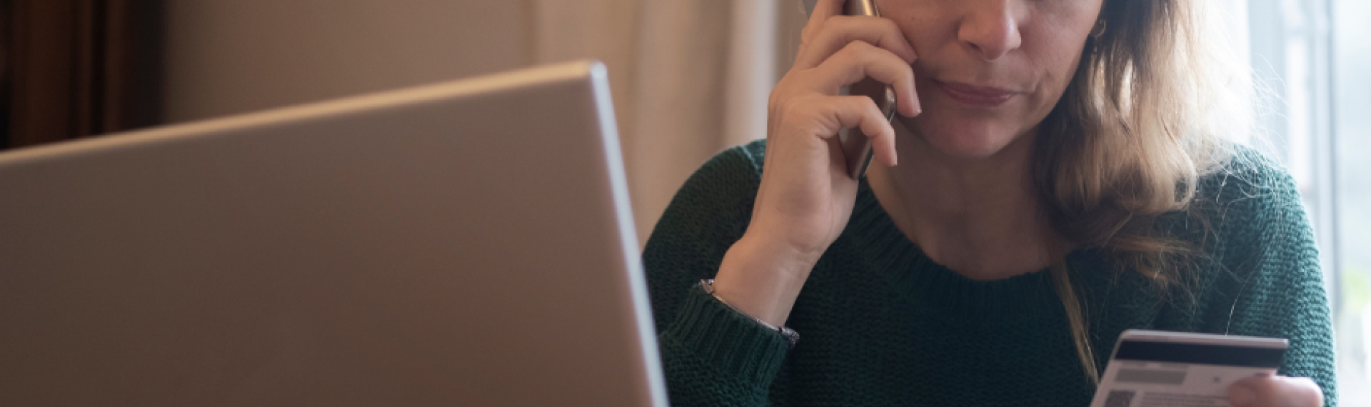 A woman with a mobile phone to her ear holding a credit card sat next to an open laptop
