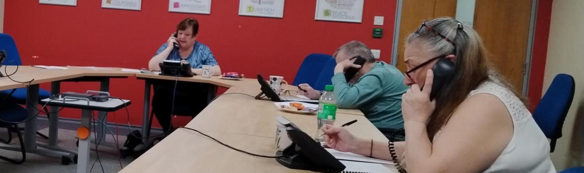 A group of people sat around a meeting table, each making a phone call on a black telephone