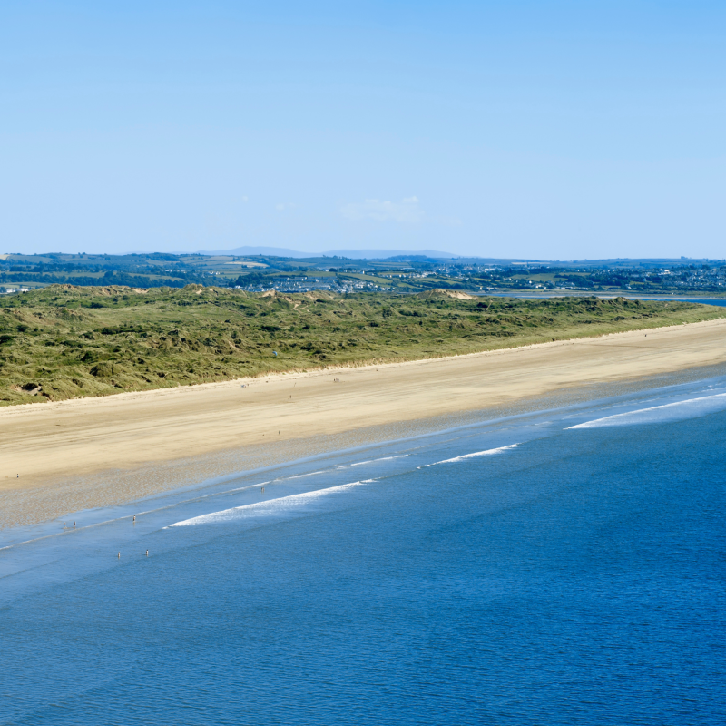Saunton Sands beach with the sea, sand and green bank behind it in the distance