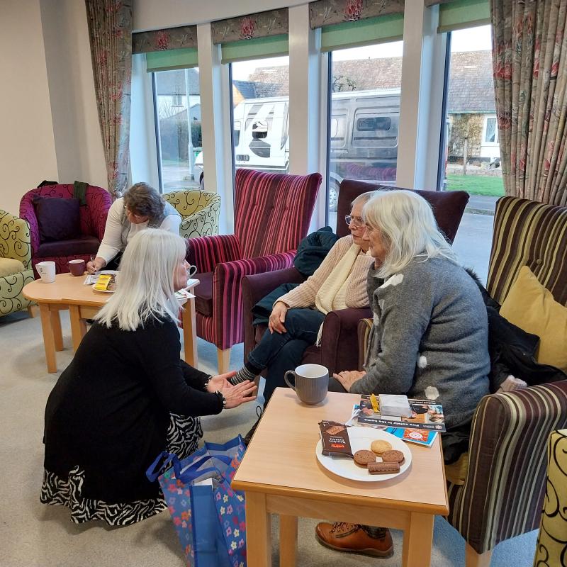 Three ladies sat on colourful armchairs with another lady crouched down on the floor talking to them