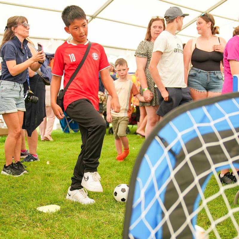 A group of children, one is about to kick a ball through a toy goal