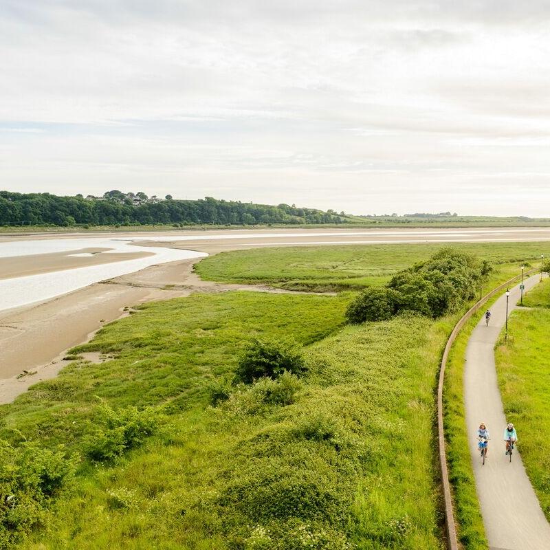A birds eye view of a cycle track next to a river at low tide