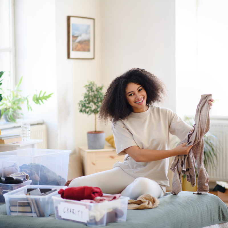 A woman with curly hair sat on a bed tidying her clothes