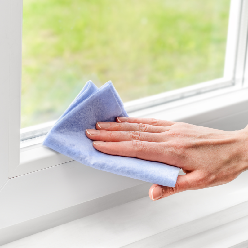 A hand holding a blue cleaning cloth and wiping a window frame