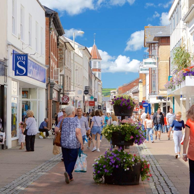 A high street in England with shops on both sides of the street and shoppers walking in the middle