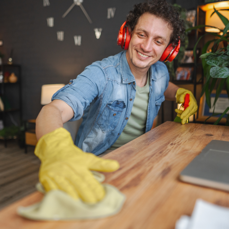 A man wearing red headphones smiling as he dusts a wooden desk