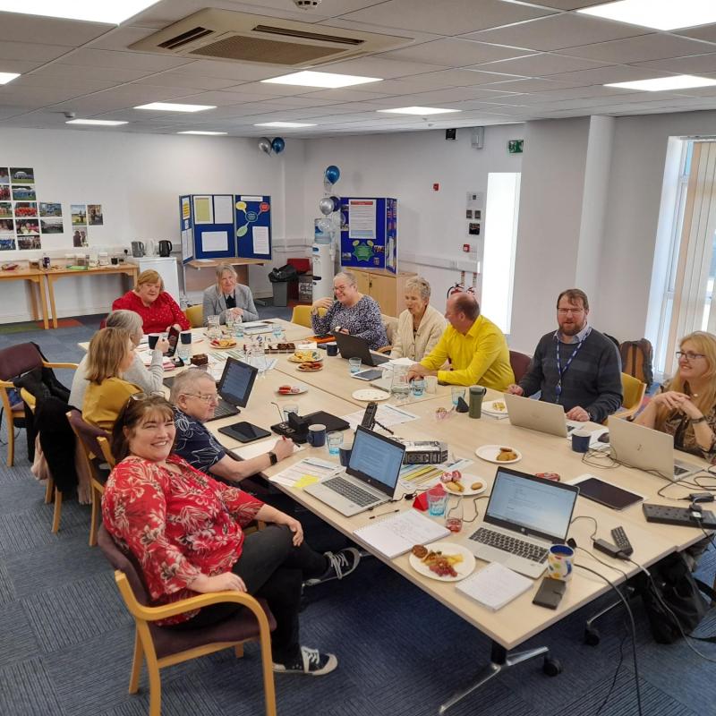 A group of people sat around a meeting table with laptops and snacks