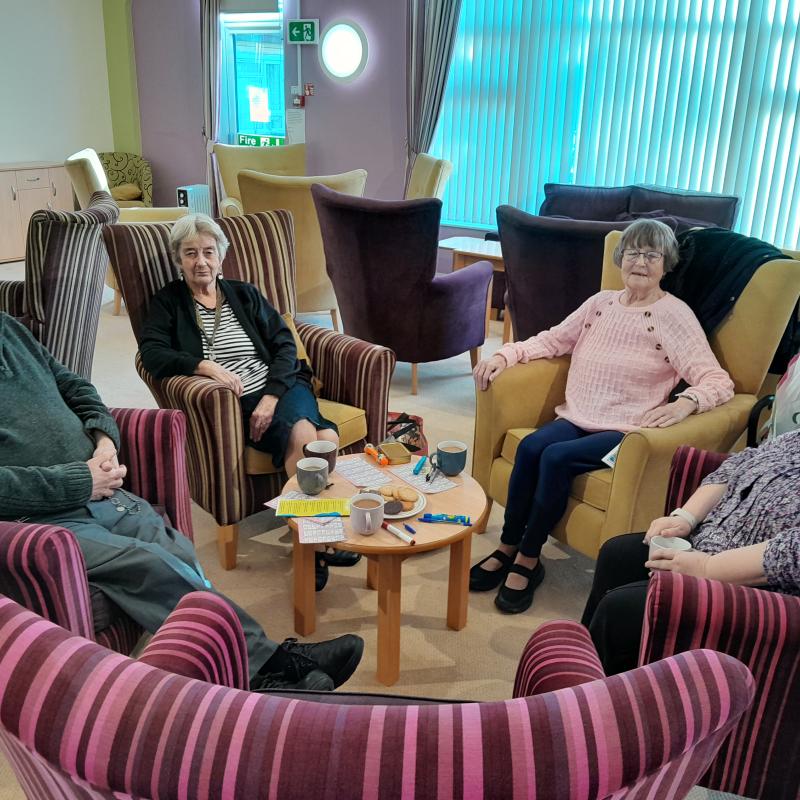A group of elderly people sat in armchairs arranged in a circle