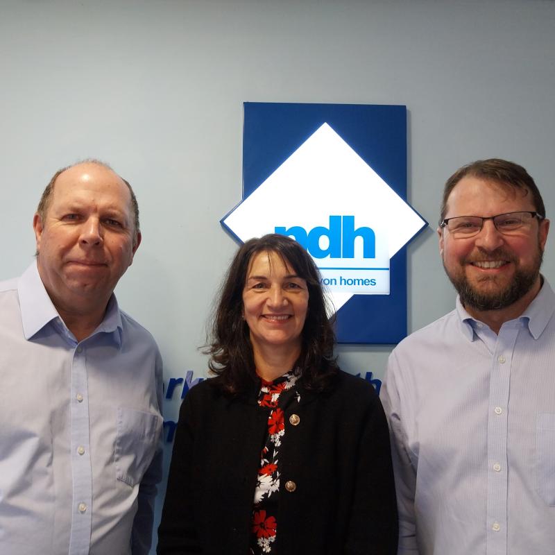 A woman standing between two men in front of an NDH sign