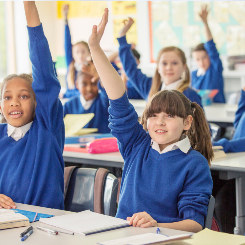 Primary school children with hands up to answer questions